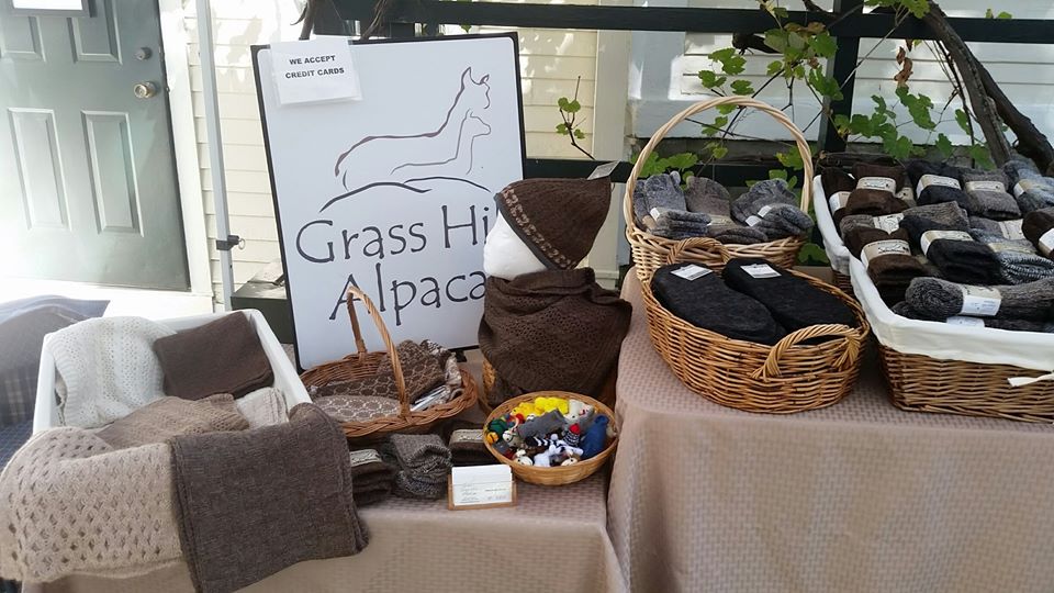 Wicker baskets of alpaca socks and folded scarves on a wooden back porch with the Grass Hill Alpacas wooden sign and hanging vines